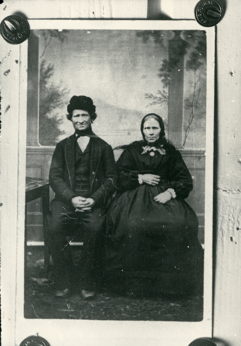 Fotografi festet på treplate med tegnestifter. Mann og kvinne, sittende, antagelig fra før 1900