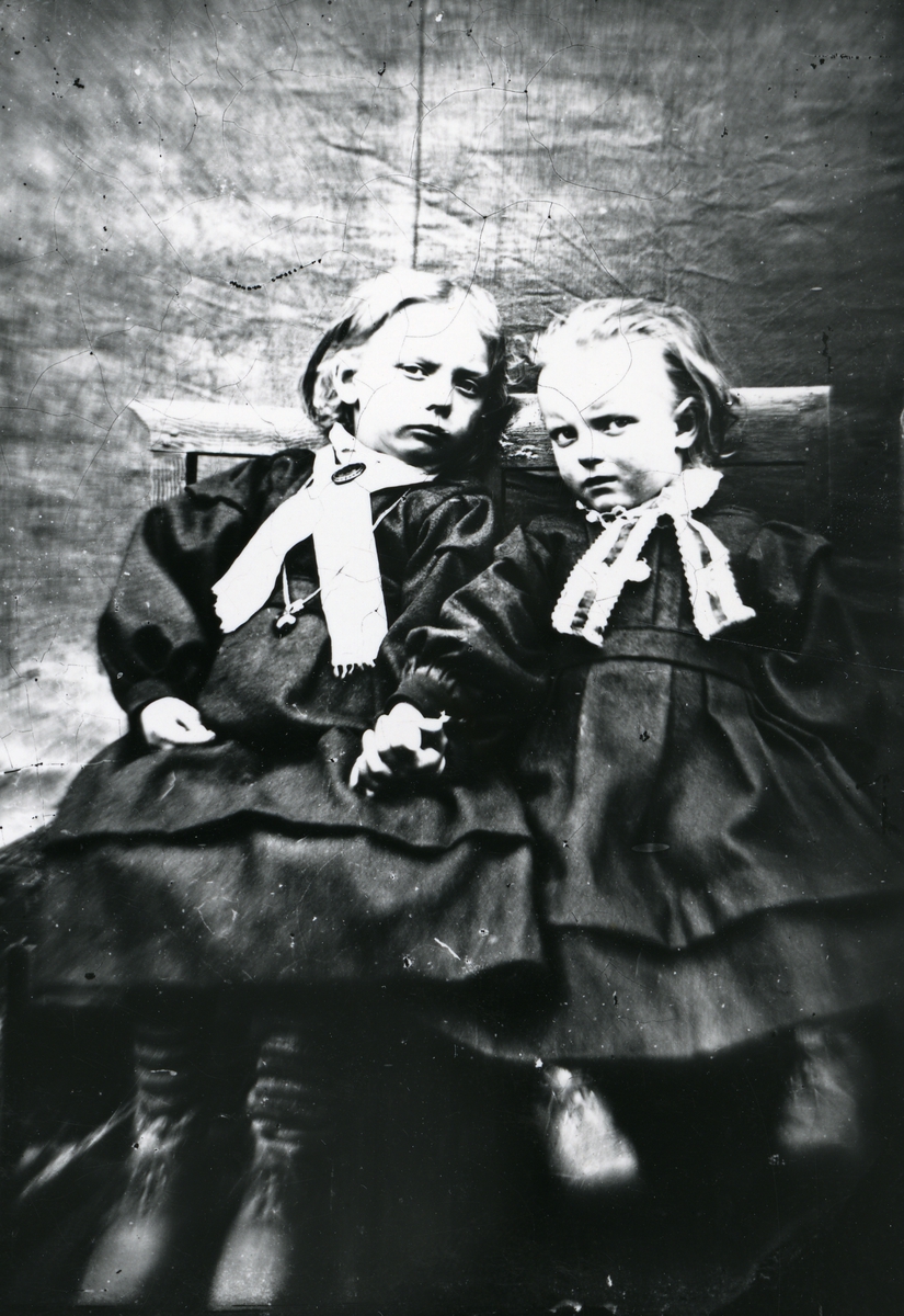 To barn i kjoler, sittende på stol
