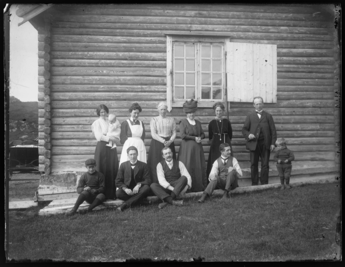 Ei gruppe mennesker fotografert i husveggen ved turnhytta på Skagen. I bakerste rekke fra venstre er fru Grasmo nr. 4. Ytterst til høyre står Grasmo
