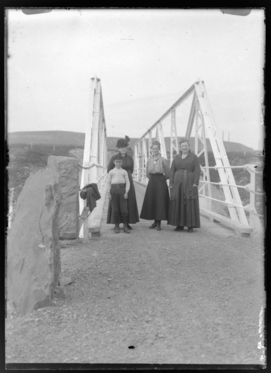 Tre kvinner og en gutt på broa over Komagelva. Fru Grasmo til venstre.