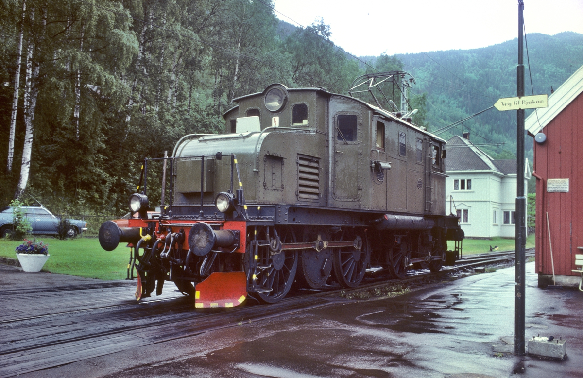 Rjukanbanens elektriske lokomotiv RjB 14 på Mæl stasjon. Skilt viser vegen for reisende til Rjukan. Norsk Hydro, Norsk Transportaktieselskap, Norsk Transport.