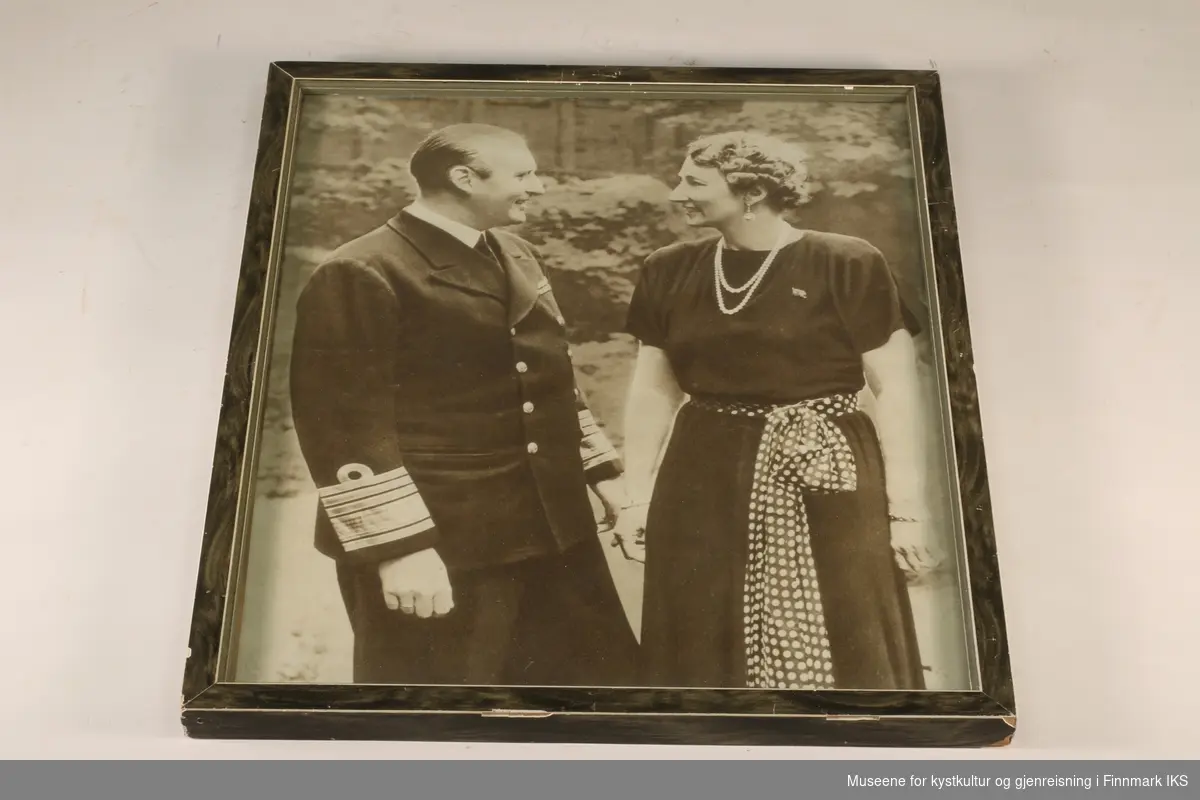 Kronprins Olav (ikledd uniform) og Kronprinsesse Märtha (lang, mørk kjole, prikket bånd knyttet på midjen, smykker). De ser på hverandre. I sort-hvitt.
