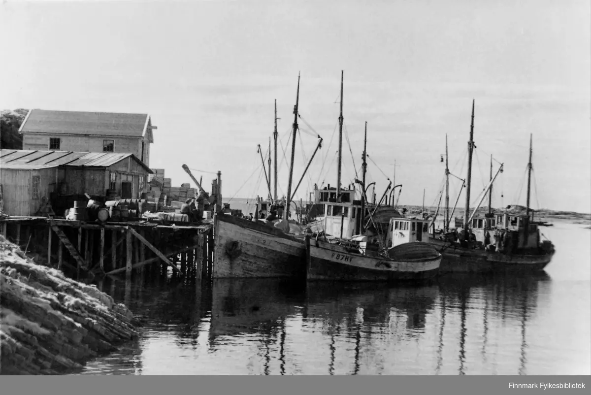 'Hasvåg på Sørøy med fiskebruket. Dette forholdsvis lille bruket hadde til 01.05.46. tatt imot 140 tusen kg. fisk.' Tre-fire båter ligger ved kaia som er full av tønner og esker.