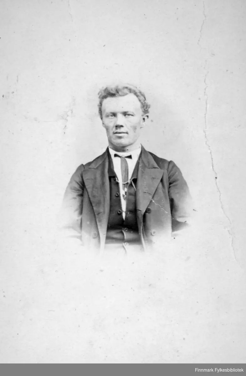 Portrett av en mann. Han har mørk dressjakke, mørk vest under, hvit skjorte og slips. Portrettet er tatt hos fotograf M. Koefoed.