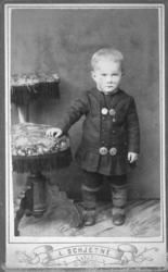 Portrett av en ung gutt. Har har en mørk jakke med fire stor