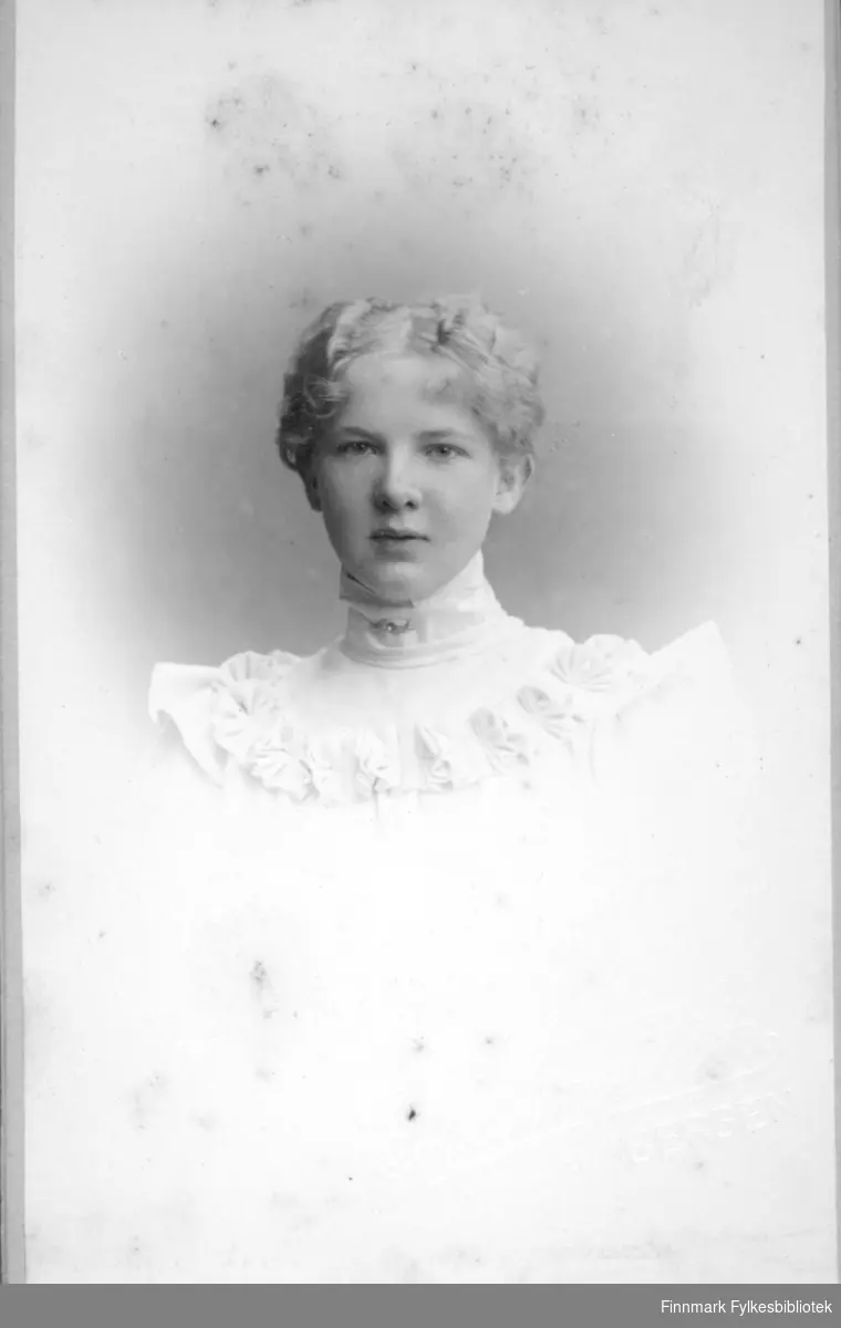 Portrett av en ung kvinne kledt i en lys eller hvit kjole med høy krage og en blondekant rundt øvre del av brystet.