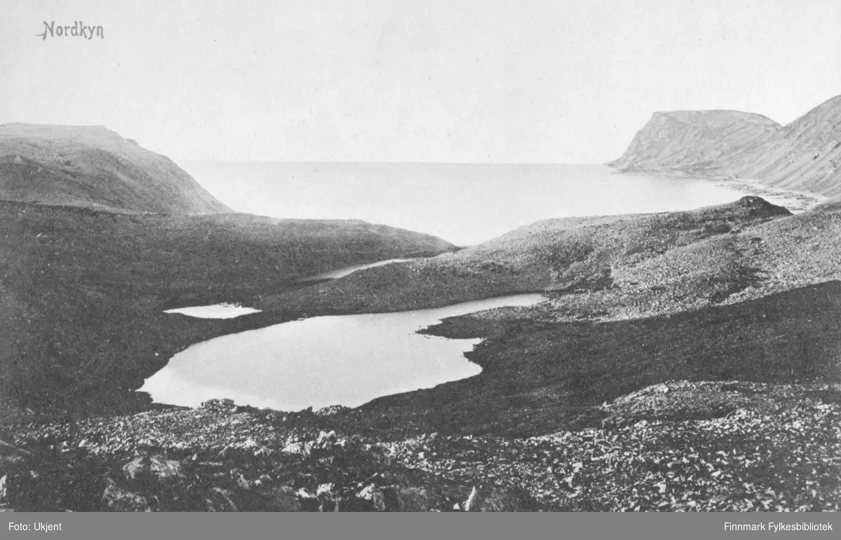 Et postkort med landskapet i Nordkyn som motiv. På bildet kan man se en innsjø i en dal, omringet av fjell. Lengre ut kan man se havet.