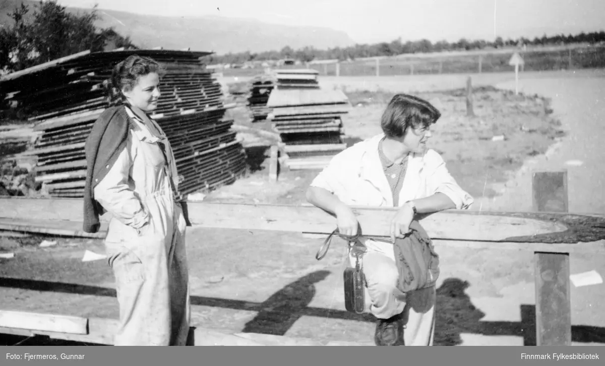 To kvinner fotografert ved gjerdet på Banak flystasjon i Lakselv en sommerdag. Persoene er ukjente og bildet er tatt i august 1946.