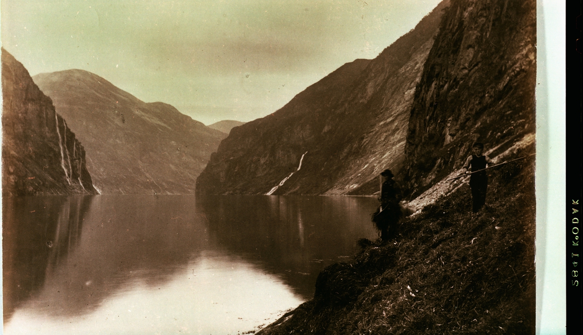 To personer raker høy ved Geirangerfjorden. Fossen "De syv søstre" i bakgrunnen?