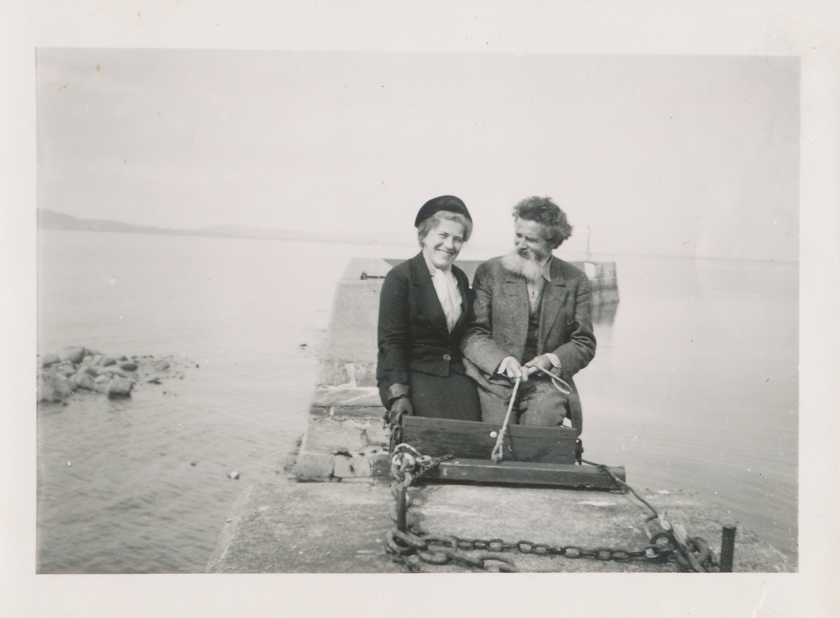 En mann og kvinne sitter på en molo ved sjøen.