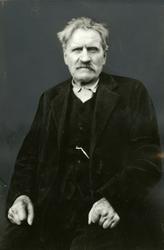 Portrett av en eldre mann. Mannen er iført en mørk dress.