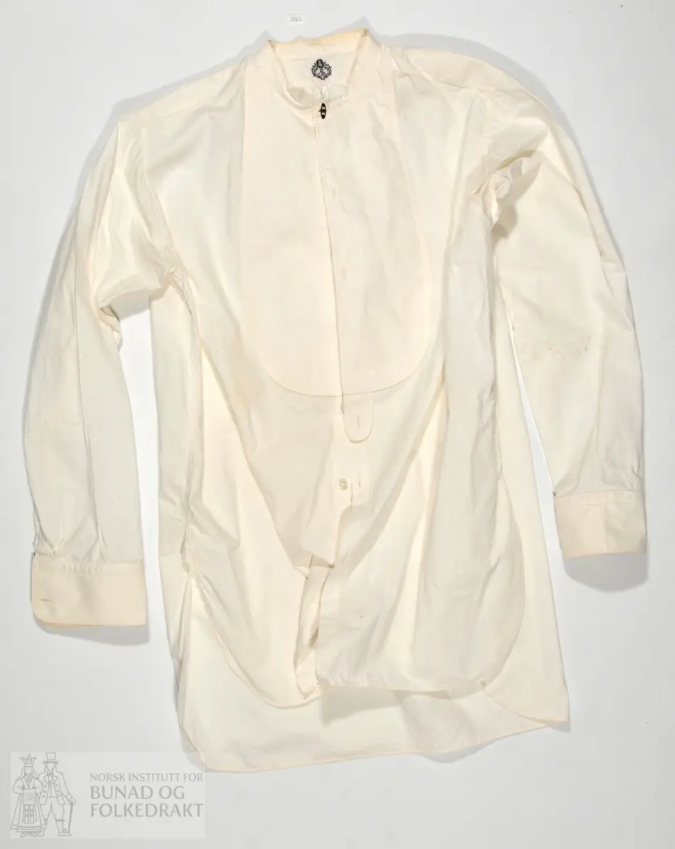 Skjorte kjøpt på butikk, med merkelapp i nakken AL 1898. Stiva skjortebryst. Maskinsydd. 85cm midt bak og ned.