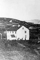 Våningshus. Folk oppstilt foran røystveggen, og flagg bak hu