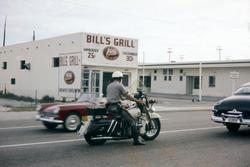 Politimann på motorsykkel. Burgersjappe i bakgrunnen.