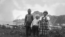 Gruppebilde av tre barn, med hjeller(?) og fjell i bakgrunne