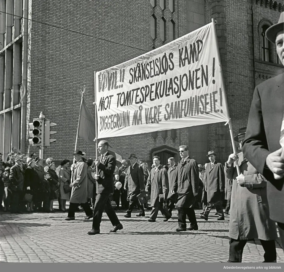 1. mai 1964 i Oslo.Demonstrasjonstoget i Karl Johans gate.Parole: Vi vil!! Skånselsløs kamp mot tomtespekulasjonen! Byggegrunn må være samfunnseie!