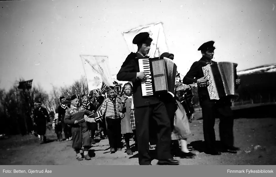 17.mai feiring ved Seida skole i 1956. Barnetåget går fra skolen, foran tåget går to menn og spiller trekkspill. Mennene fra venstre:lærer Reinen og vaktmester Andreassen fra Seida skole.