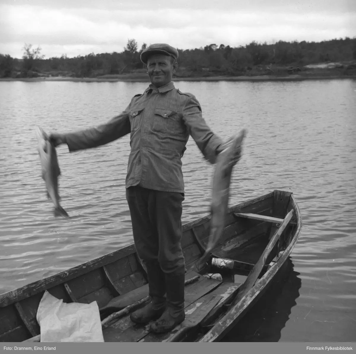 Uuno Lappalainen står i midten av en robåt og holder to store fisker i hendene.