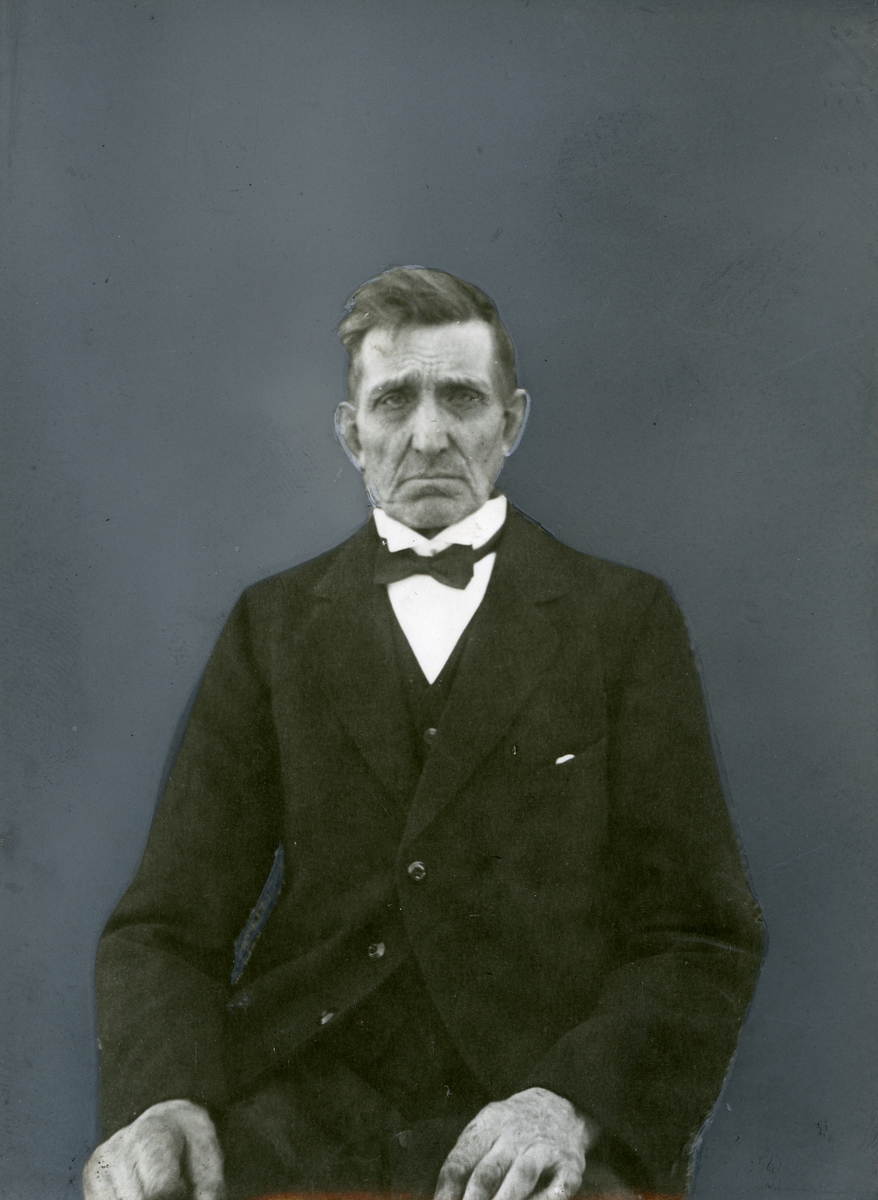 Portrett av sittende mann iført dress og sløyfe.