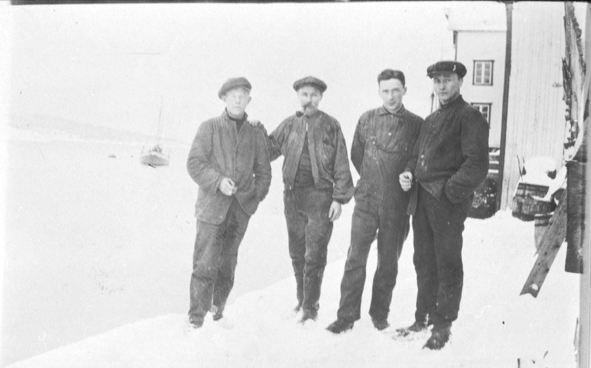 Fire menn i arbeidsklær på snødekket kai utenfor Hindø Canning.