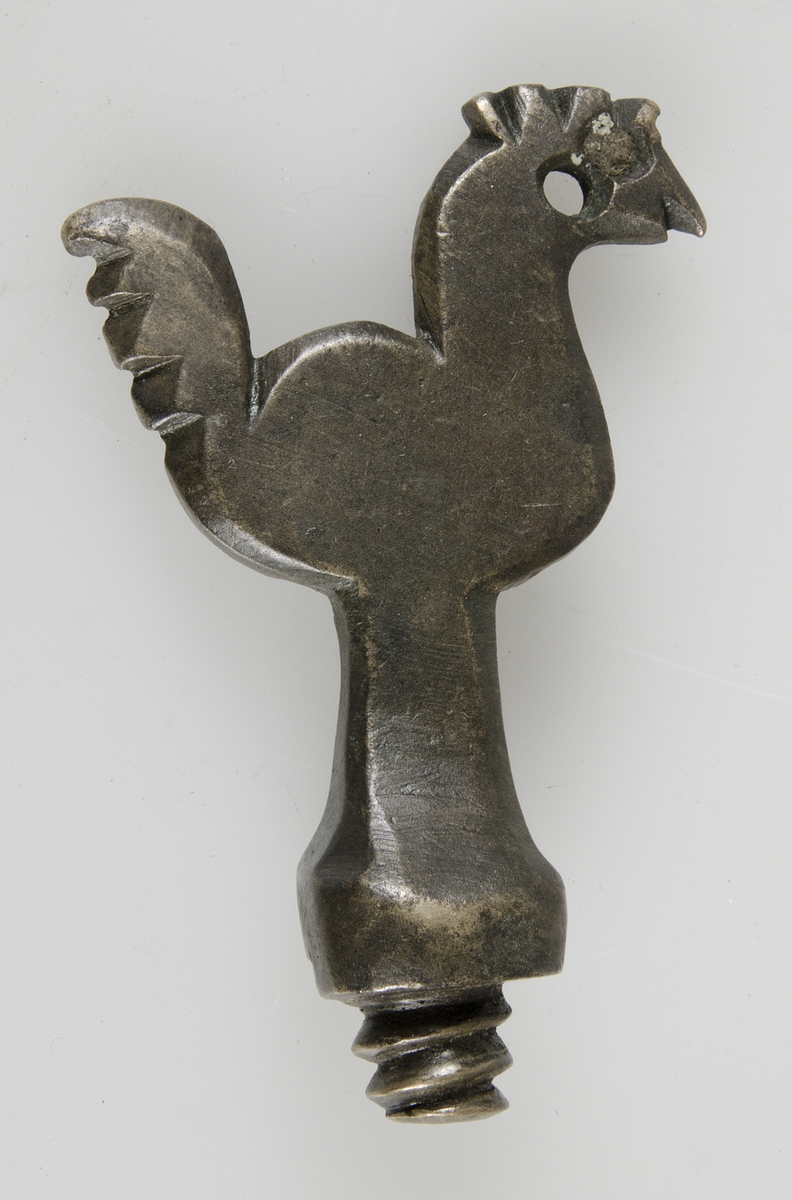 En gängad tappkran i brons, i form av en tupp.

