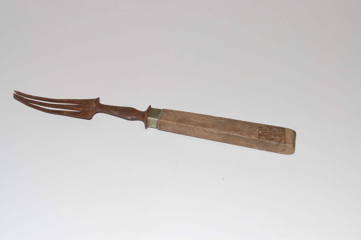 Form: Lang gaffel med tre tinder. Firkantet skaft i tr med et stykke metall av kobberlegering over seg. Stålet over skaftet / på øverste del av håndtaket er dekorativt utformet.
