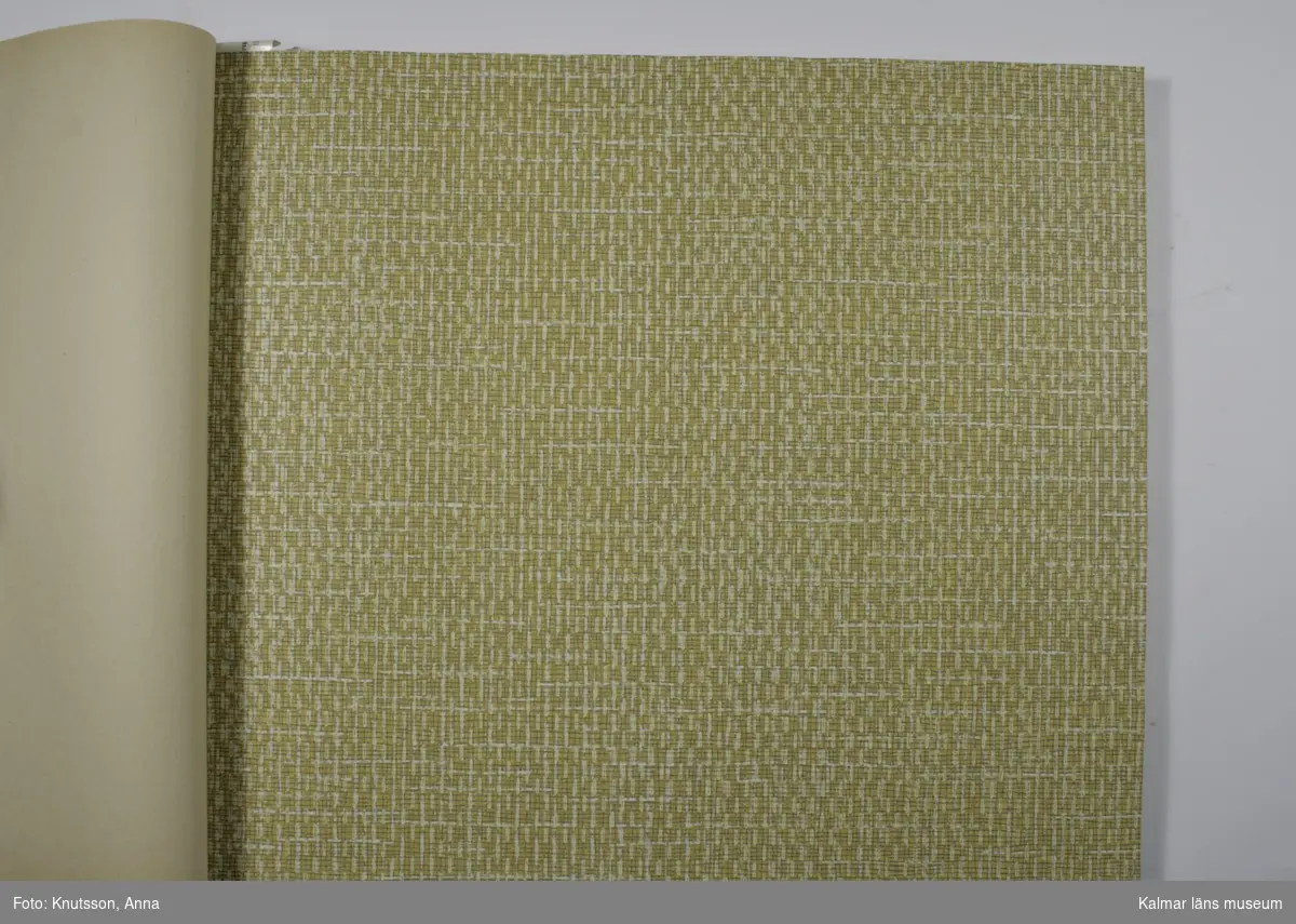 KLM 33296. Tapetkatalog. Vit, gul och grön pärm i plast med fotografi av en byggnad. Tapetkatalog för Kalmar Nya Tapetfabrik, innehåller många olika prover av tapeter från 1970-talet.