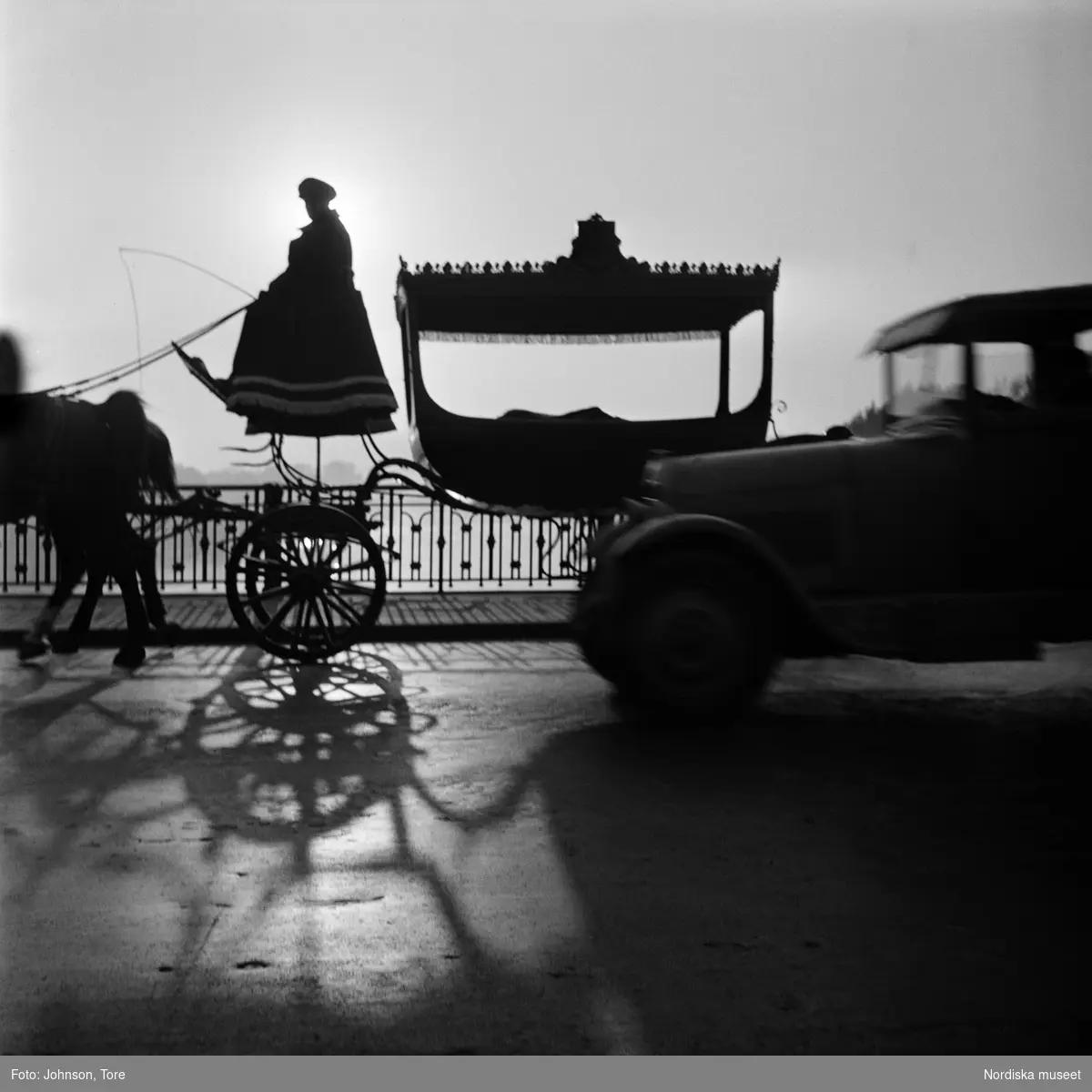 Paris. Hästdragen vagn (begravningsvagn?) med kusk i motljus på en bro. Bil i förgrunden.