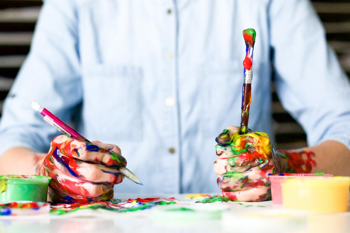Bildet viser en mann som maler og tegner, med masse malingssøl på hendene (Foto/Photo)