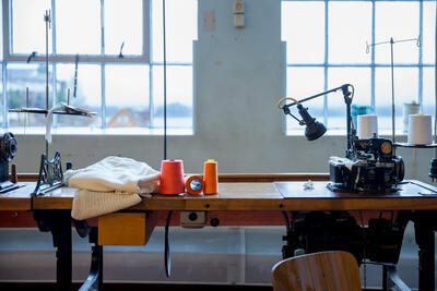 symaskin på trebord i fabrikklokale, oransje og raud sytråd. Foto/Photo