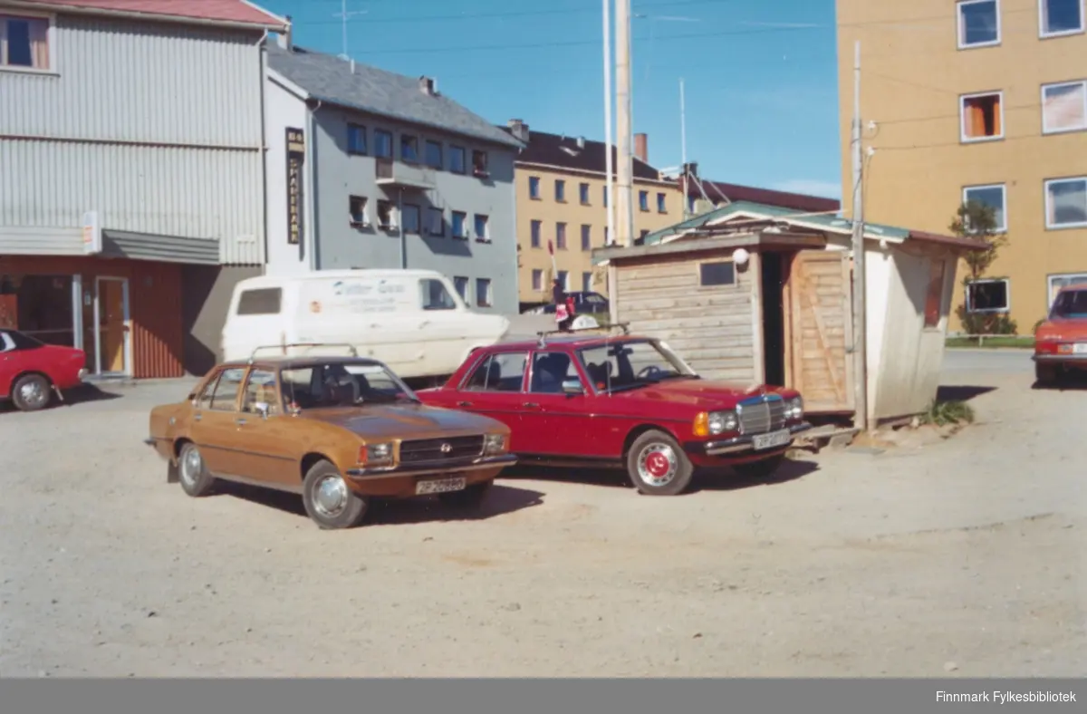 Vadsø sentrum i ca. 1976. Bjørn Dahls drosje (en rød Mercedes-Benz). I bakgrunnen ser vi bank, hotell og rådhuset.