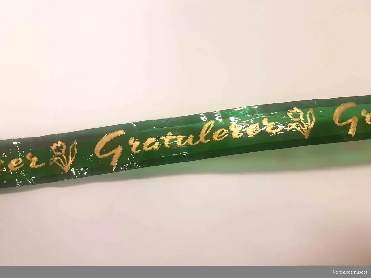 Gavebånd i grønt plastmateriale med teksten "gratulerer" i gullskrift og bilde av en tulipan.