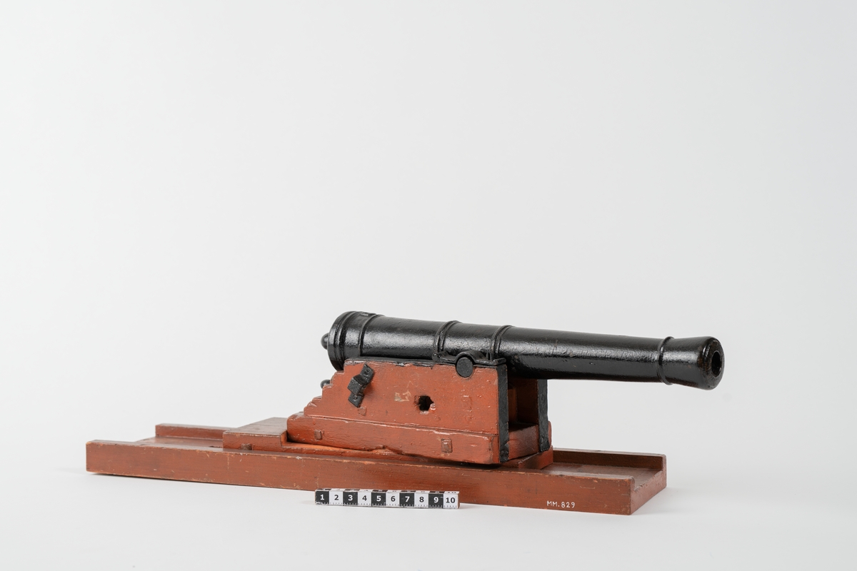 Kanonmodell: galérlåda med släde, beslagen, samt kanon. Lavetten av trä, rödmålad. Kanonen av järn, svartmålad. Tillbehör: 1 st ställhult. Lavetten L = 440 mm B = 110 mm H = 130 mm.