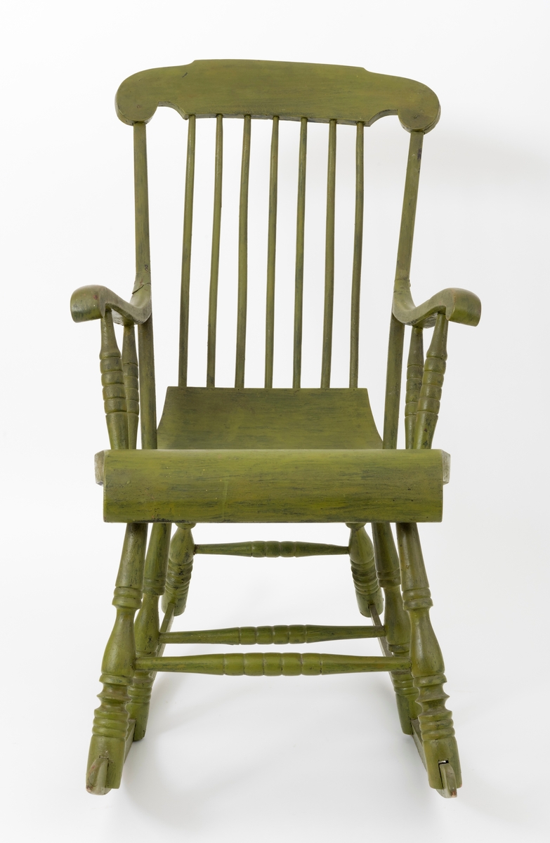 Stol, gyngestol, med seks ben på to meier. Stolen er påført grønn farge, sannsynligvis oppå en opprinnelig svart farge. (Setet er på undersiden svartmalt.) Konstruksjonen kan minne om slik pinnestolene er sammenføyd. Bena er dreid og tappet inn under setet. De to meiene er felt inn i (opp i) utskårne spalter i stolbena. Det er dreide sprosser, mellomstykker, mellom hvert benpar, foran, på midten og bak.  Setet buer nedover i framkant, og oppover i bakkant. Stolen har sju trespiler i ryggen som er tappet i setet og toppstykket. Armlenene er delvis felt inn i ryggstolpene (rygstavene). Armlenene er forsterket med metallbeslag. Det er to dreide sprosser (støtteben) under hvert armlene, disse er tappet inn i armlenet og setet. Toppstykket på stolryggen er felt inn i  og skrudd fast til ryggstolpene (ryggstavene) på stolryggen. Stolryggens ryggstolper er tappet ned i setet.