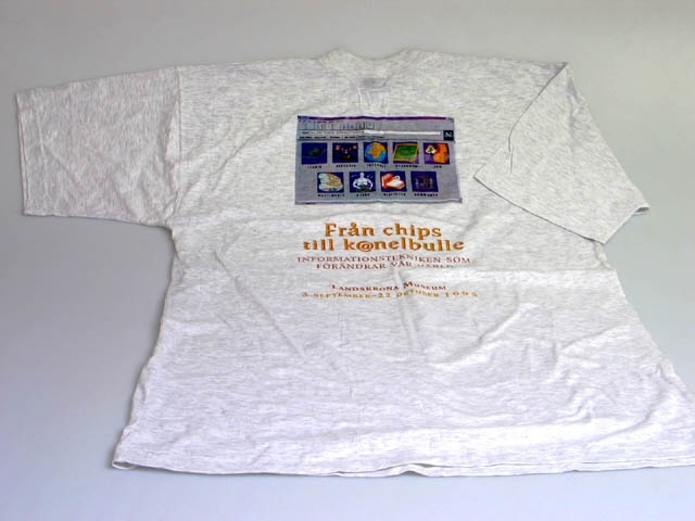 Grå T-shirt som använts som marknadsföring av en utställning på Landskrona museum. På ryggen finns en bild av ett datorskärmsfönster med möjlighet till olika sökalternativ. Undertill står texten: "Från chips till k@nelbulle. INFORMATIONSTEKNIKEN SOM FÖRÄNDRAR VÅR VÄRLD. LANDSKRONA MUSEUM, 3 SEPTEMBER-22 OKTOBER 1995". Tröjan är i storlek XL och på lappen i nacken står "BEST FASHION, QUALITY BRAND, Plaza, SILVER", samt tvättråd.