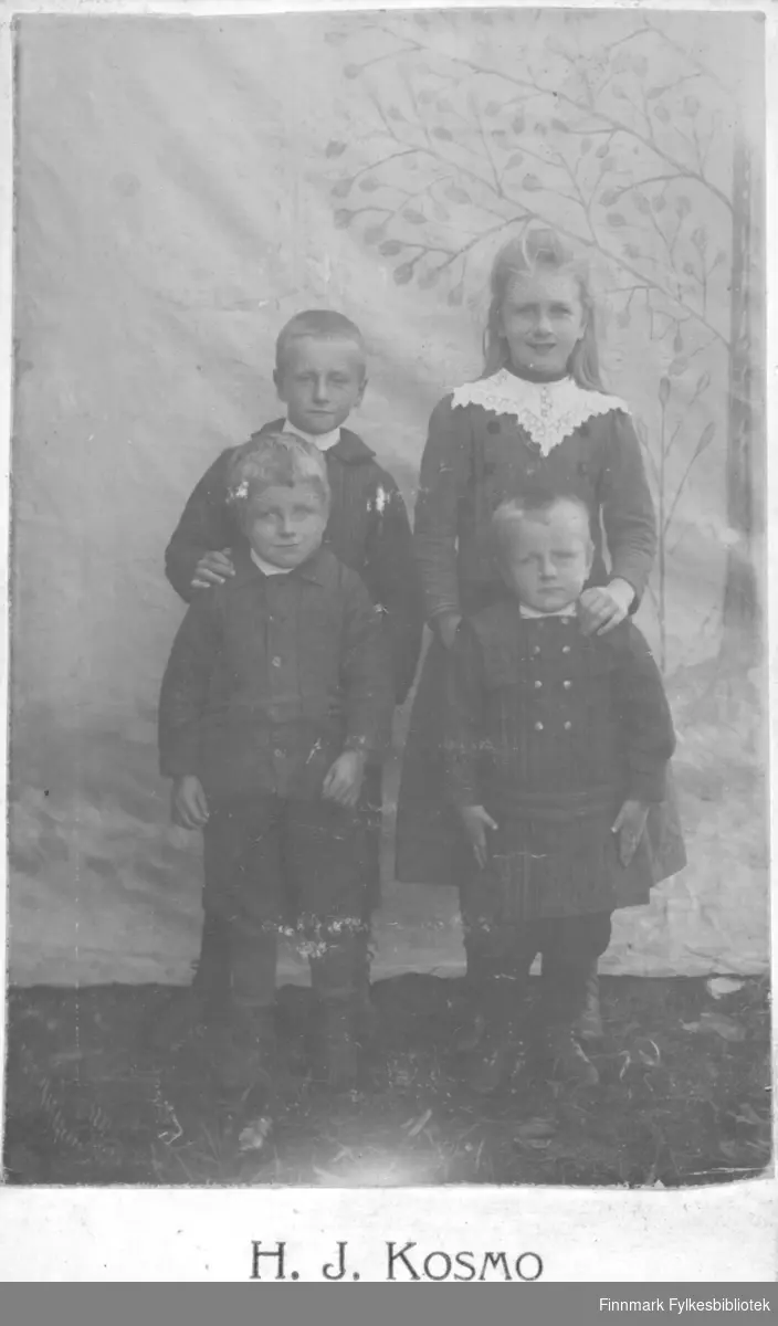 Fire barn kledd i finklær fotografert i fotoatelier til Hans Jensen Kosmo. Hans Jensen Kosmo var fotograf og tok bilder på Fuske i Stokke fra omkring 1895 til 1900.