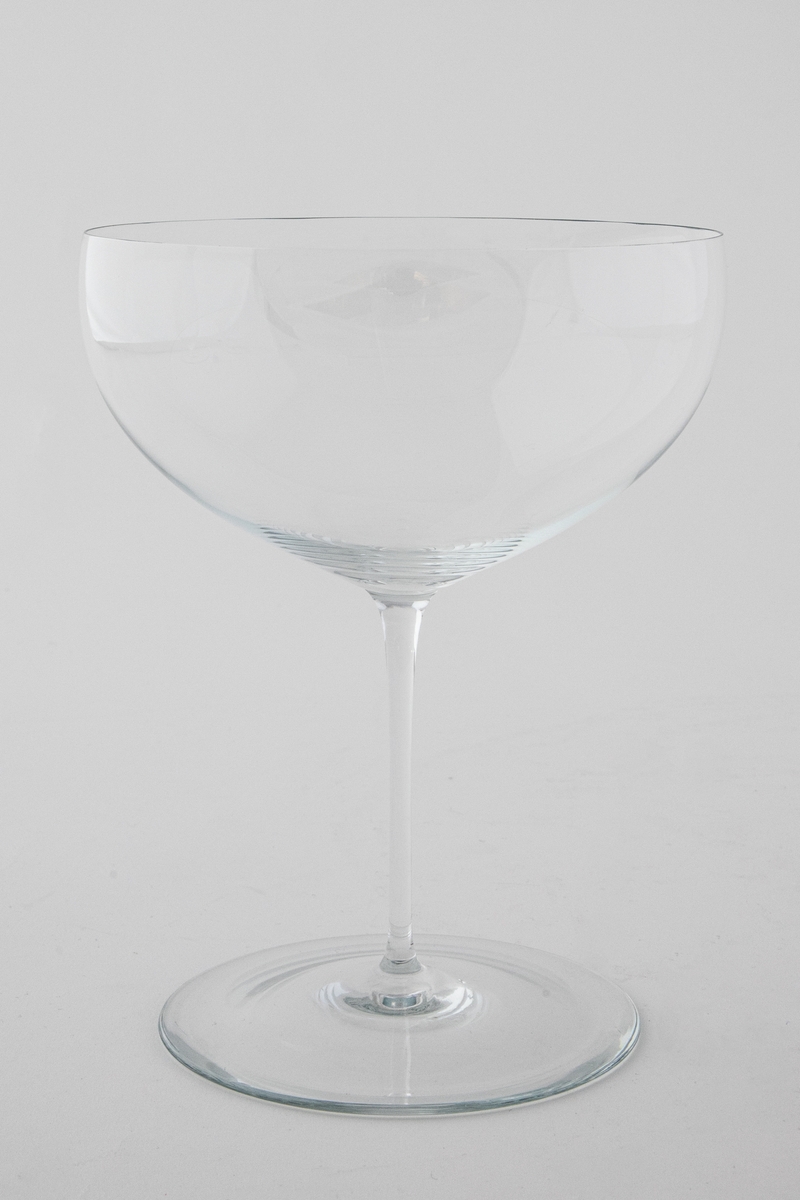 Cognacglass i meget tynt klart glass. Vid kupa som bæres av en meget tynn stett. Sirkulær fotplate, noe hevet på midten.