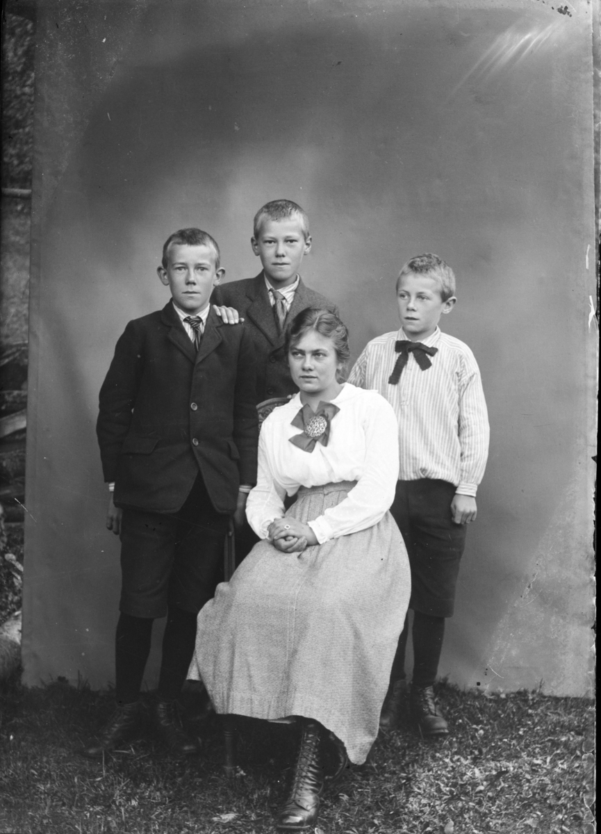 Ung jente, kanskje med tre yngre brødre. Portrett tatt utendørs med laken bak.