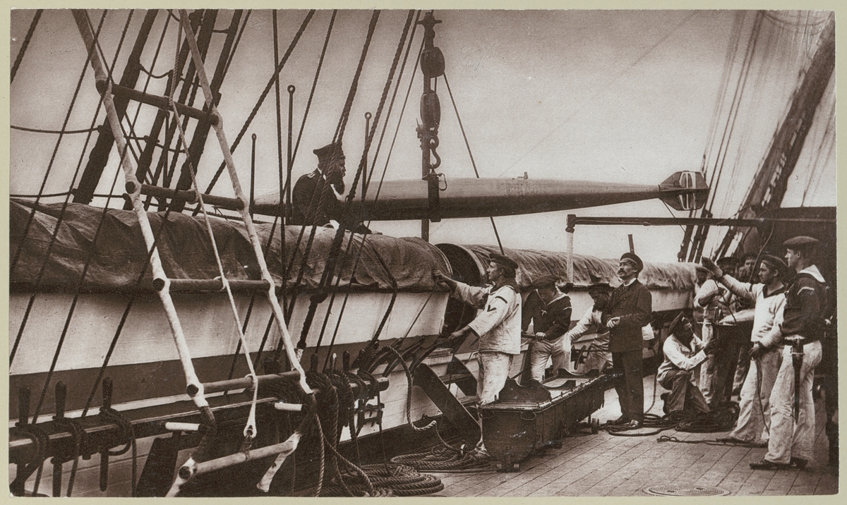 Bilden förställer tyska sjömän ombord på korvetten Stosch som drillas i hanteringen av torpeder på däcket. Här lyftas torpeden över bord för skjutning.