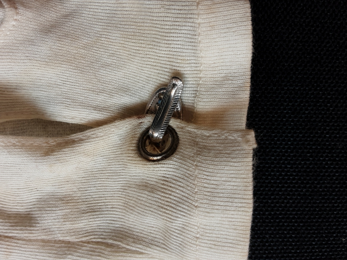 Hanske. Høyre. Hvit bomull, splitt på innsiden av håndleddet som lukkes med metallspenne. Tre maskinbroderte hvite striper på handbaken.