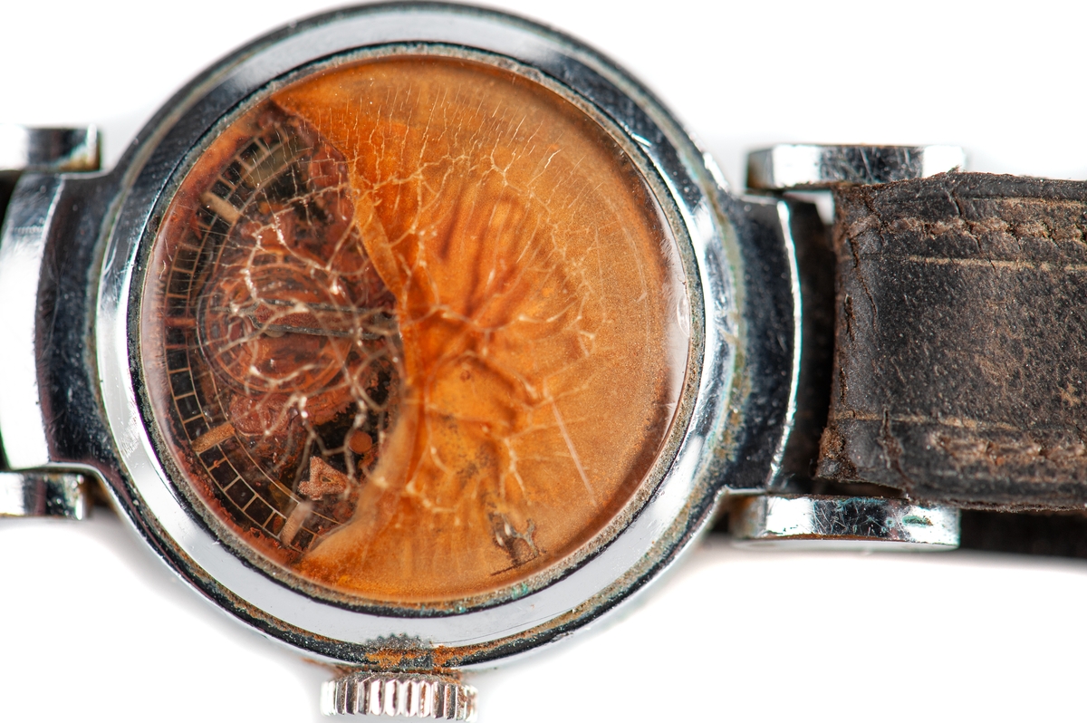 Armbandsur med brunt läderarmband. Rostangripen urtavla bakom bukigt krackelerat glas.