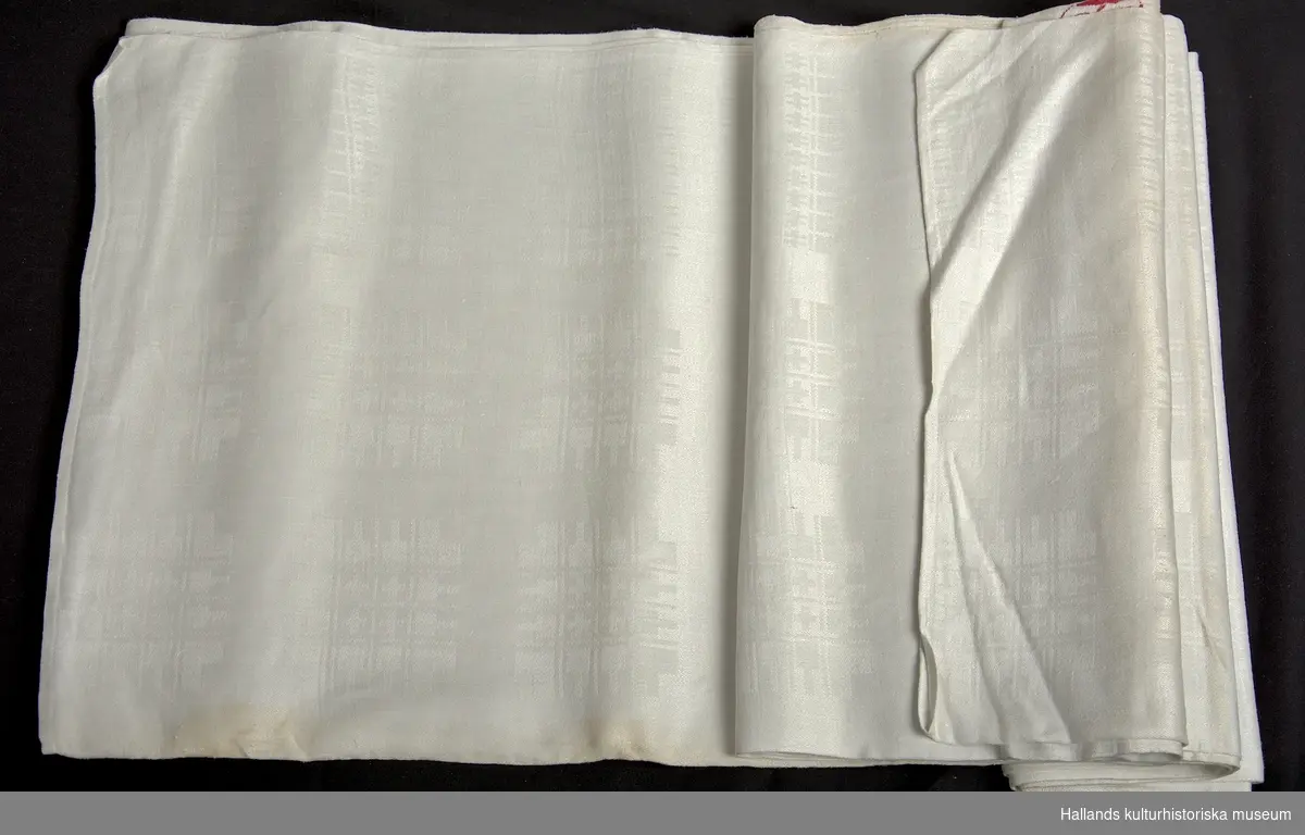 En vit lunneduk med tillhörande linneservetter.  Samtliga föremålen har en dekor bestående av geometriska mönster och bär ett broderat monogram: "AB" (Anna Bagge).