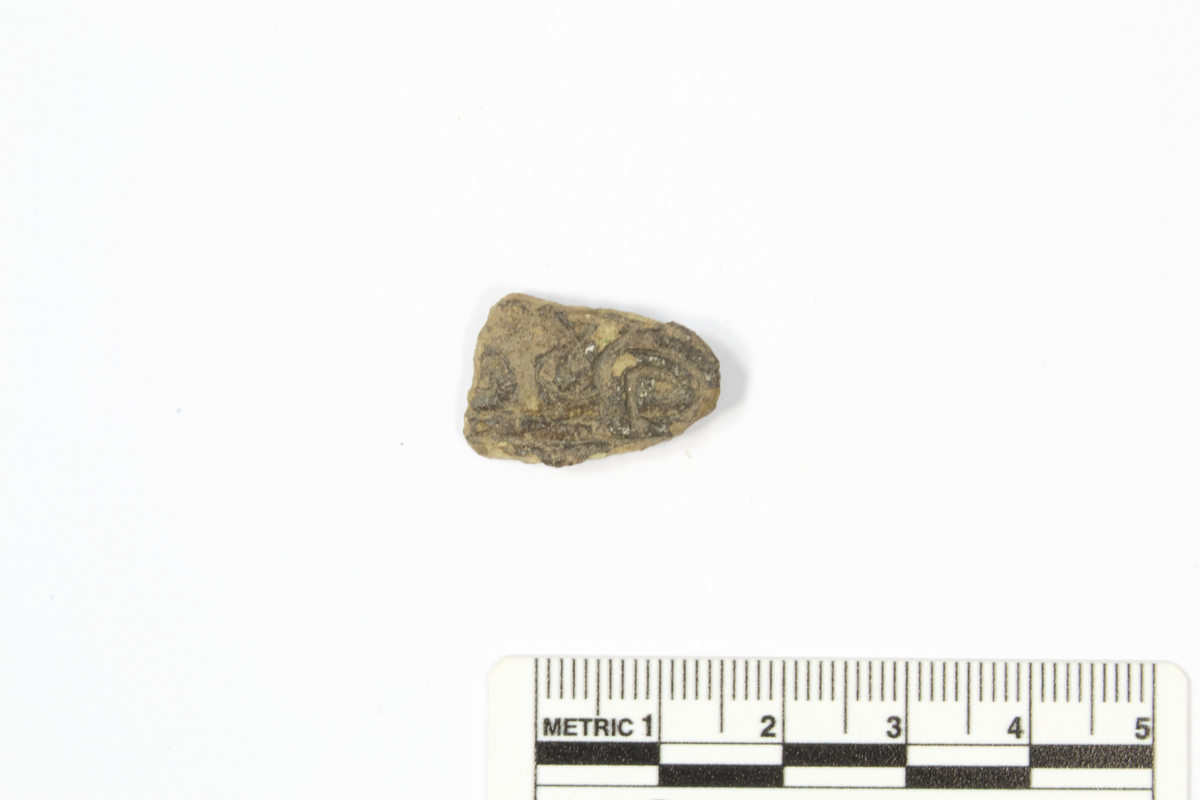 Spenne, fragment med rester av dekorert forside og bevart rest av nålefeste på baksiden, Stl. 21 mm og Stt. 2 mm.