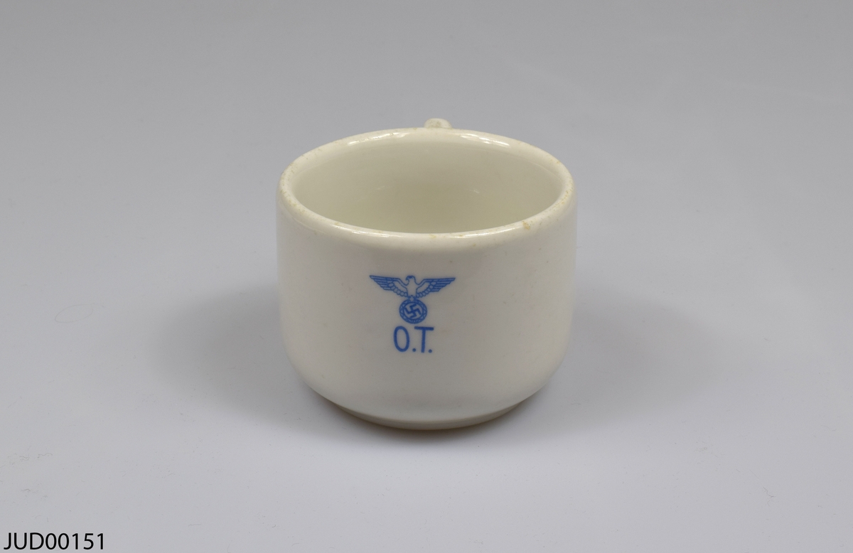 Kopp med tillhörande fat, tillverkade av vitt porslin. Både koppen och fatet är dekorerad med en nazistisk örn hållandes swastika och initialerna O.T i blått. Tillverkade i Norge.