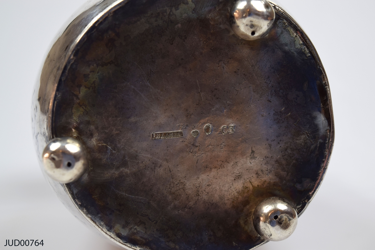Insamlingsbössa från 1809, tillverkad av silver. Myntinkast ovanpå locket. Även vridet handtag fastsatt i locket. Nyckelhål precis nedanför lock. Inskription på hebreiska runt om. Står på tre kulfötter.