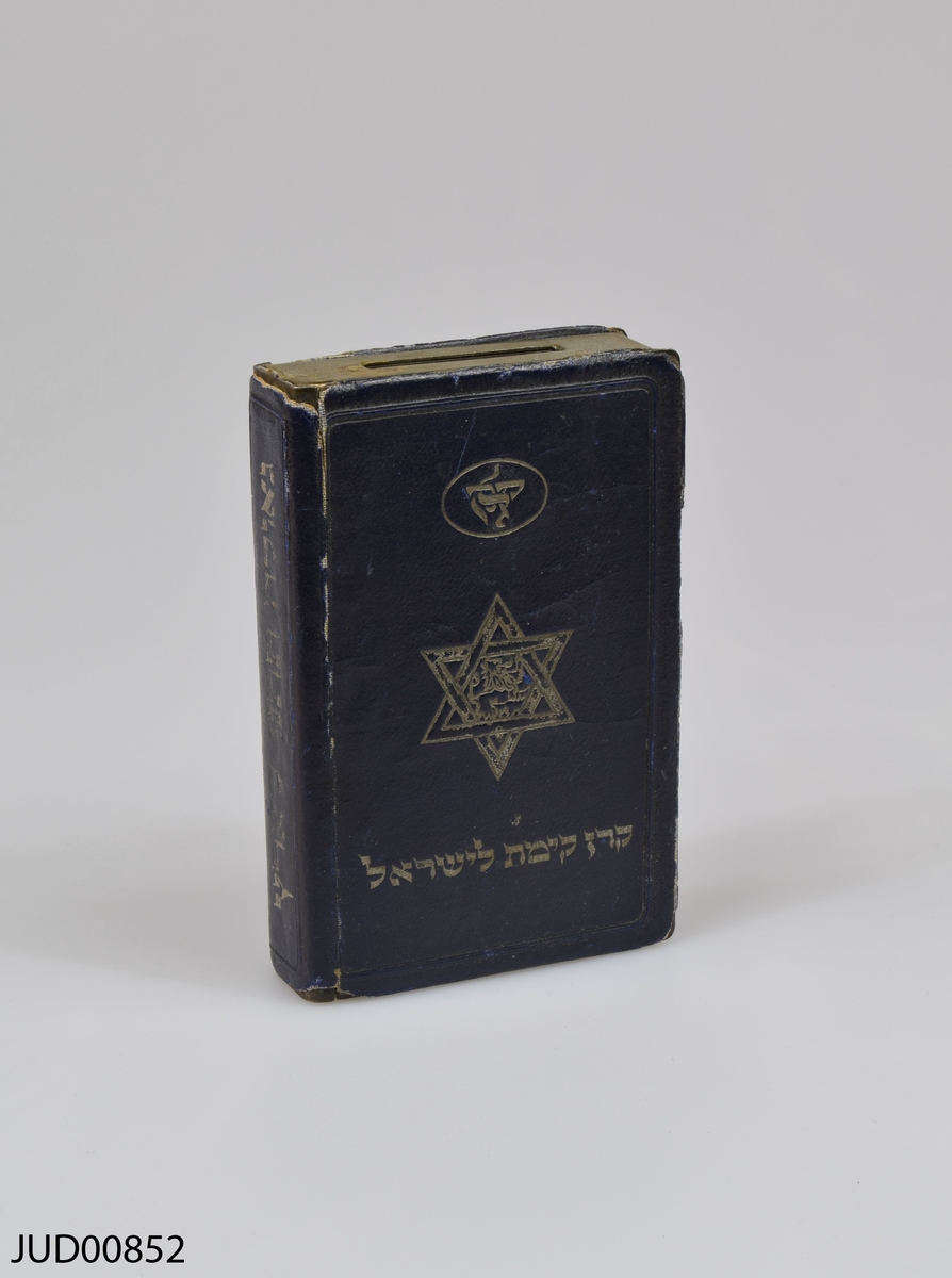 Insamlingsbössa, tillverkad av metall, i form av en bok. Hebreisk text på fram- och baksida. Karta över Israel i relief på framsidan, och en davidsstjärna på baksidan.
