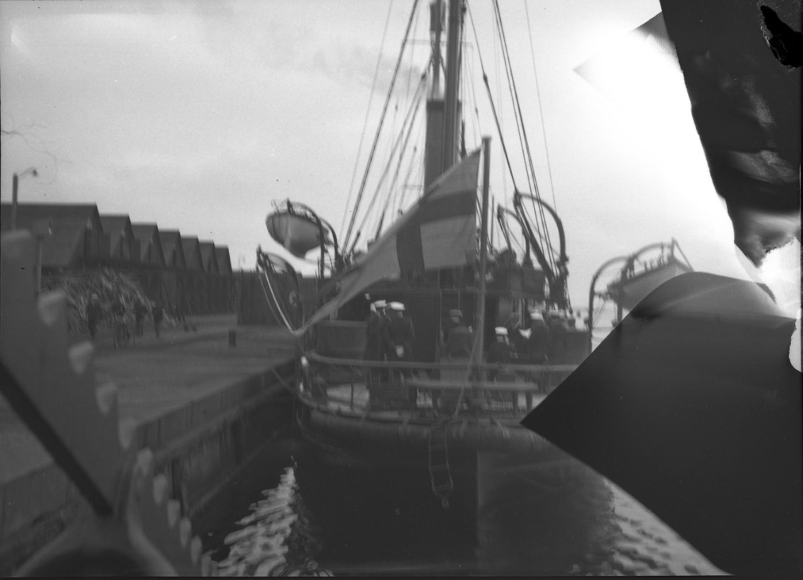 Kanonbåten HMS Svensksund vid kaj. Örlogsflaggan är hissad i aktern, där det också står ett antal officerare.
