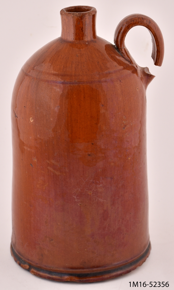 Krus, cylinderformat, av brunglaserad lera, upptill kraftigt avsmalnande, handtaget saknas.