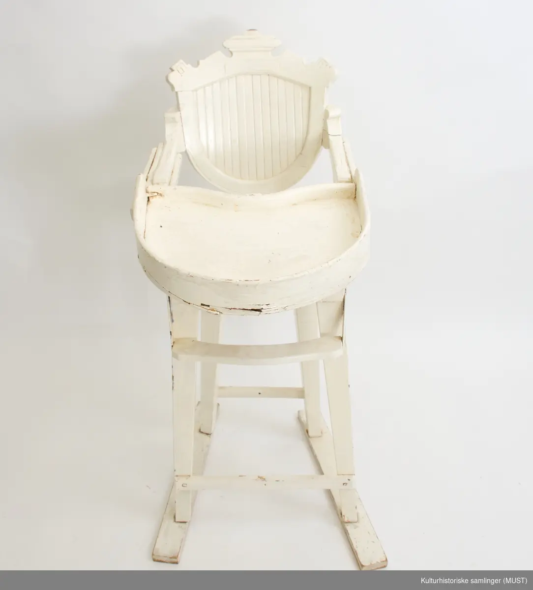 Barnestol med bordplate og fothviler. Skåret dekor i ryggen. Sekundær hvit maling. Bordplaten er forsterket på den ene siden med en lask. Sannsynligvis sekundære bein.