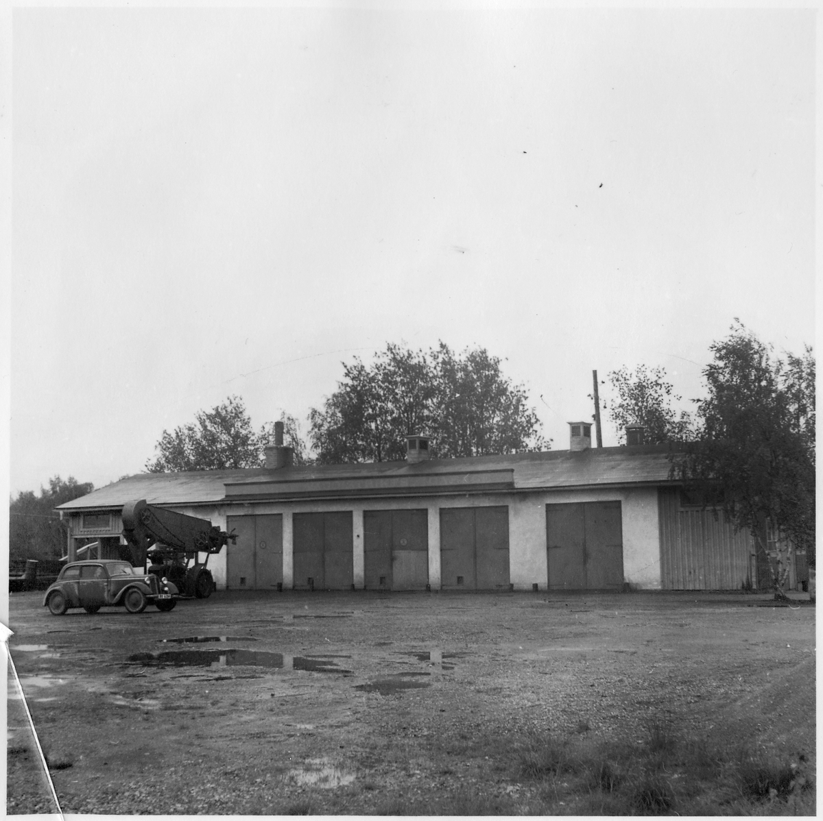 Vägstation BD6, Råneå. Garagebyggnad. Framför byggnaden lastningselevator (skopelevator) monterad på traktor, troligen tillverkad av Svedala. Personbil.